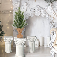 Load image into Gallery viewer, Decorative setting with classical columns, a small artificial Christmas tree, and ornate wall decorations.