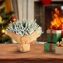 Load image into Gallery viewer, Faux Christmas tree in a burlap wrap with wrapped gifts on a wooden table in front of a fireplace.
